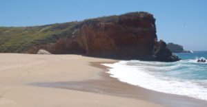 A sandy beach, waves, and tall cliff