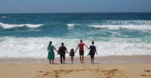 five people hold hands and walk towards ocean waves