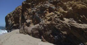 rocky cliff face rises out of a sandy beach and the ocean