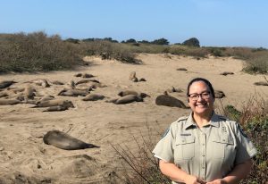 State Parks employee smiles in front of a beach full of elephant seals