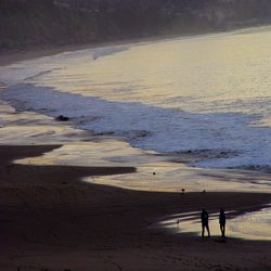 two people walk along a calm beach at dusk