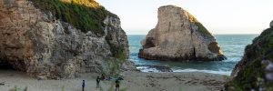 A beach alcove between coastal cliffs. A group of people stand, playing in the sand.