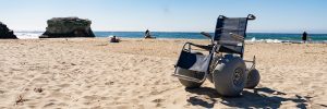 A beach wheelchair is positioned on the sand in front of the ocean