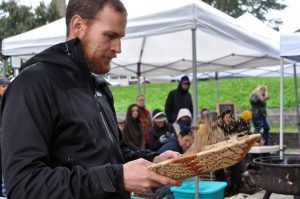 a man stands with a wooden bowl, flicking its contents in the air