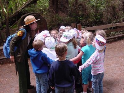 a group of small children gather around in a circle with a State Parks worker