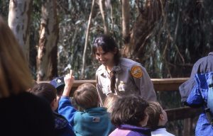 A state Parks worker talks, smiling, to a group of children