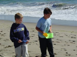 two kids hold shovels and pails in the sand on a beach