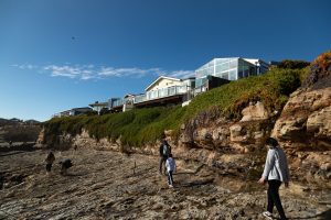 Park visitors walking in front of a short, rocky cliff with green plants growing draped over the top.