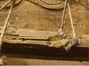 Old, fractured wood has twine fastened to it with uneven nails