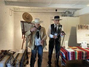 Two men dressed in ranchero garb demonstrate a lasso