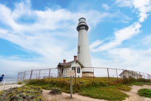 Pigeon Point Lighthouse tower standing tall against a lightly cloudy blue sky.