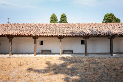 Blank side wall of Santa Cruz Mission with terracotta roof tiles, dark wooden planks and two benches pressed agains the side.