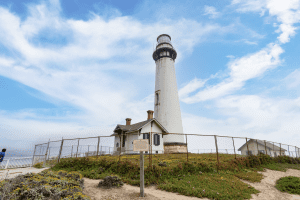 Pigeon Point Lighthouse tower standing tall against a lightly cloudy blue sky.