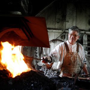 A volunteer in blacksmithing eqiupment holding metal in a fire