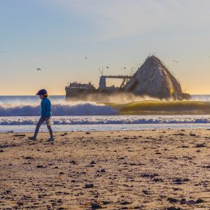 Image of cement ship at Seacliff while a kid is walking by